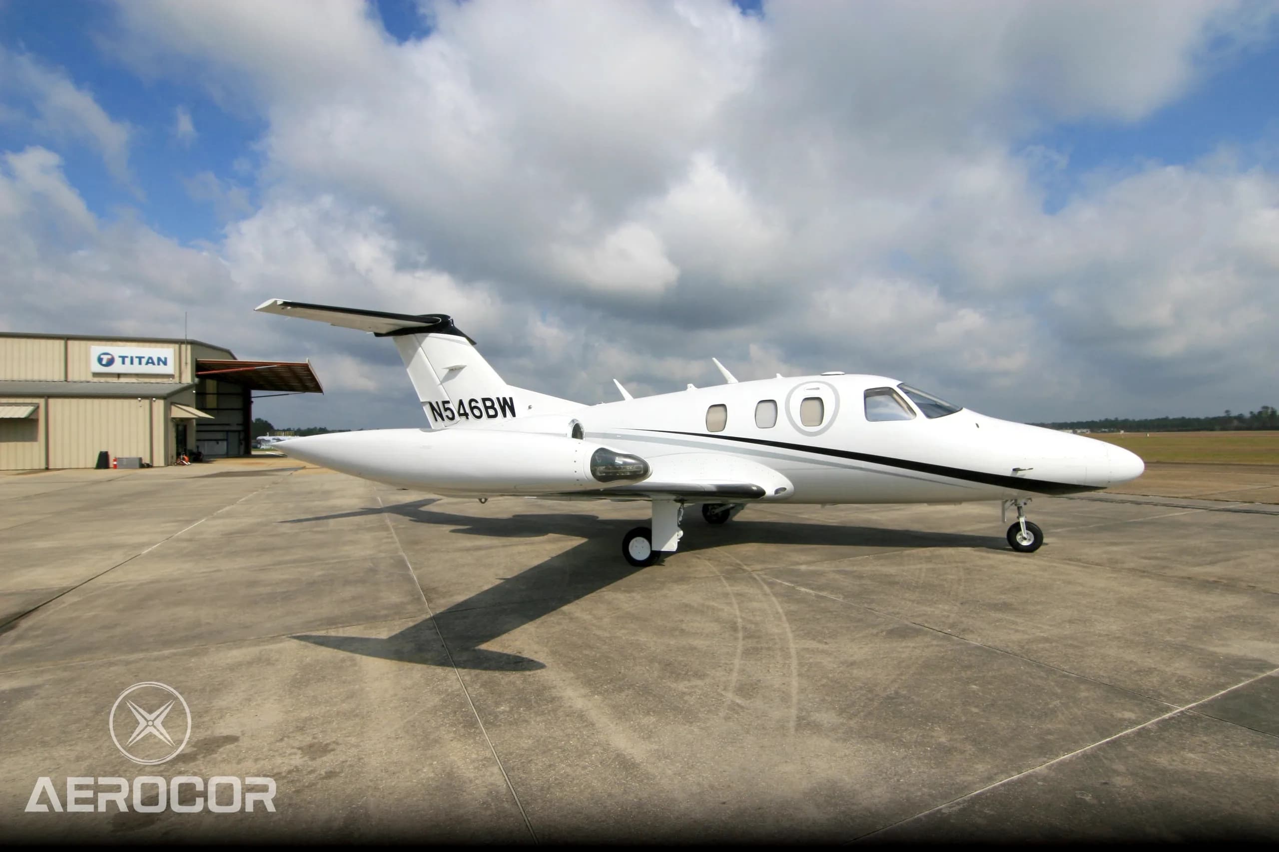 A white Eclipse 500 jet with black and grey stripes parked on an airfield, viewed from the side.