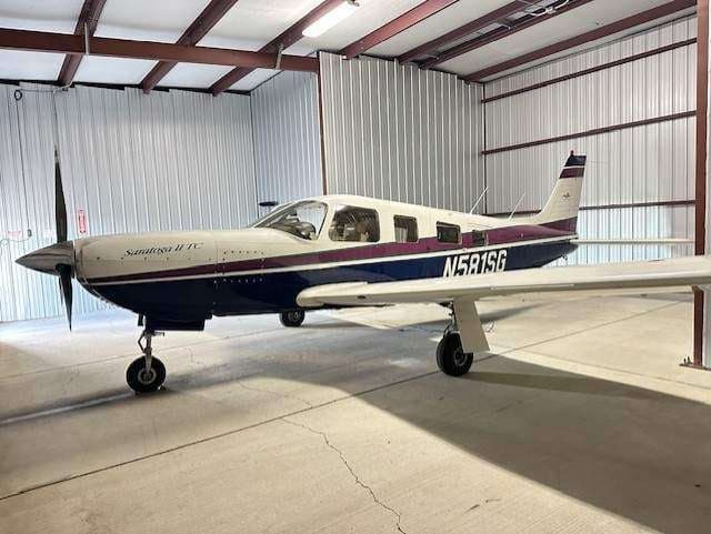 A blue, white, and purple Piper Saratoga II TC aircraft (N581SG) parked inside a hangar.