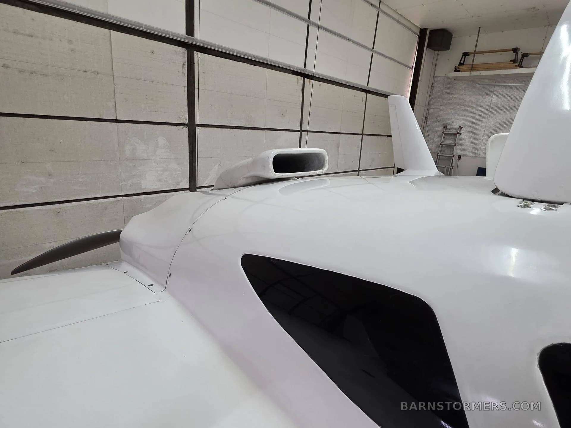 A close-up view of the white experimental aircraft's fuselage, showing the engine air intake and propeller blade.