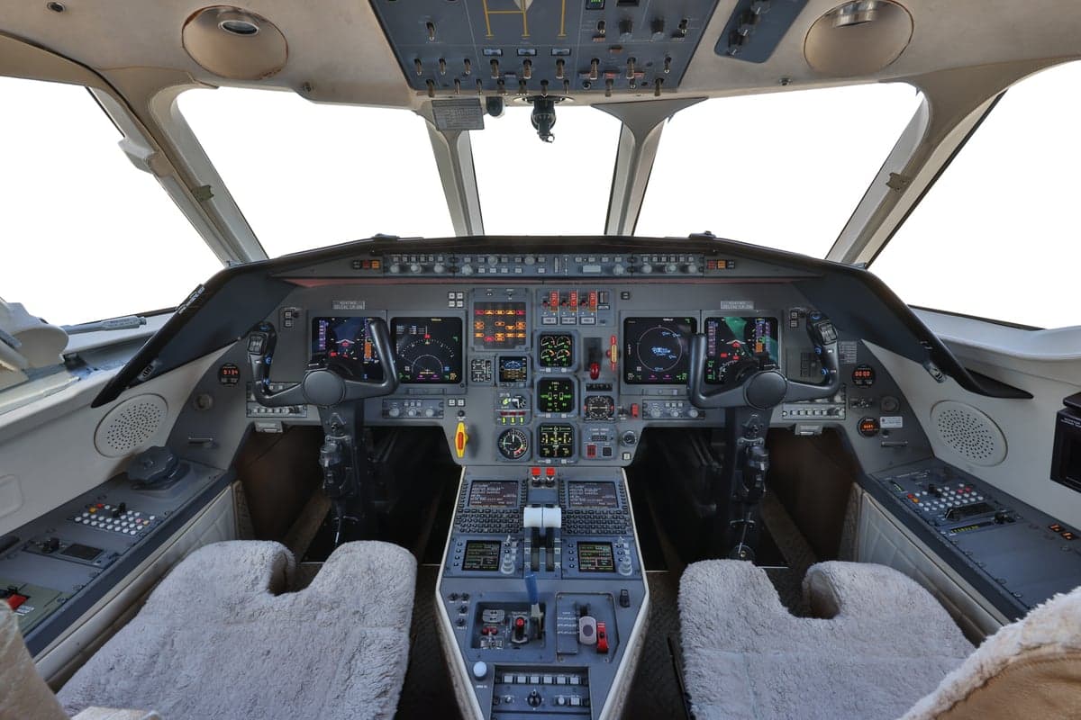 View of the aircraft cockpit with instrument panel and sheepskin seat covers.