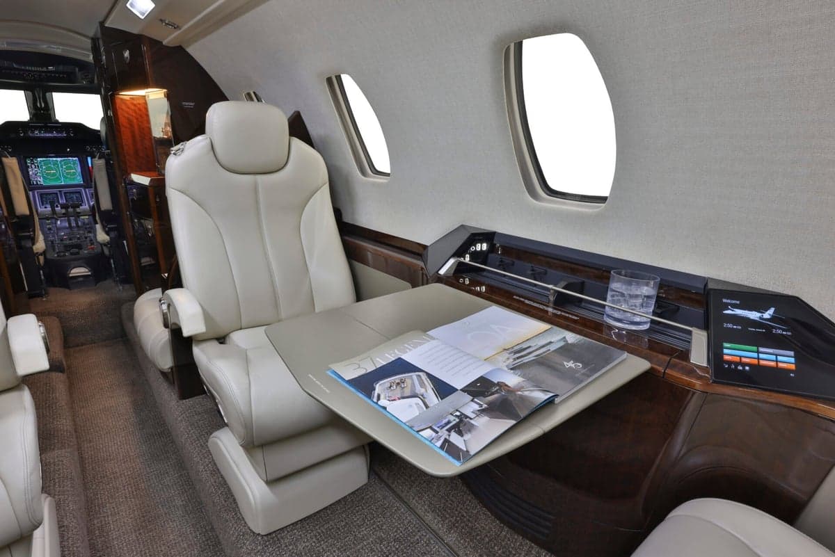 Interior view of the aircraft cabin with seats and tables facing each other.