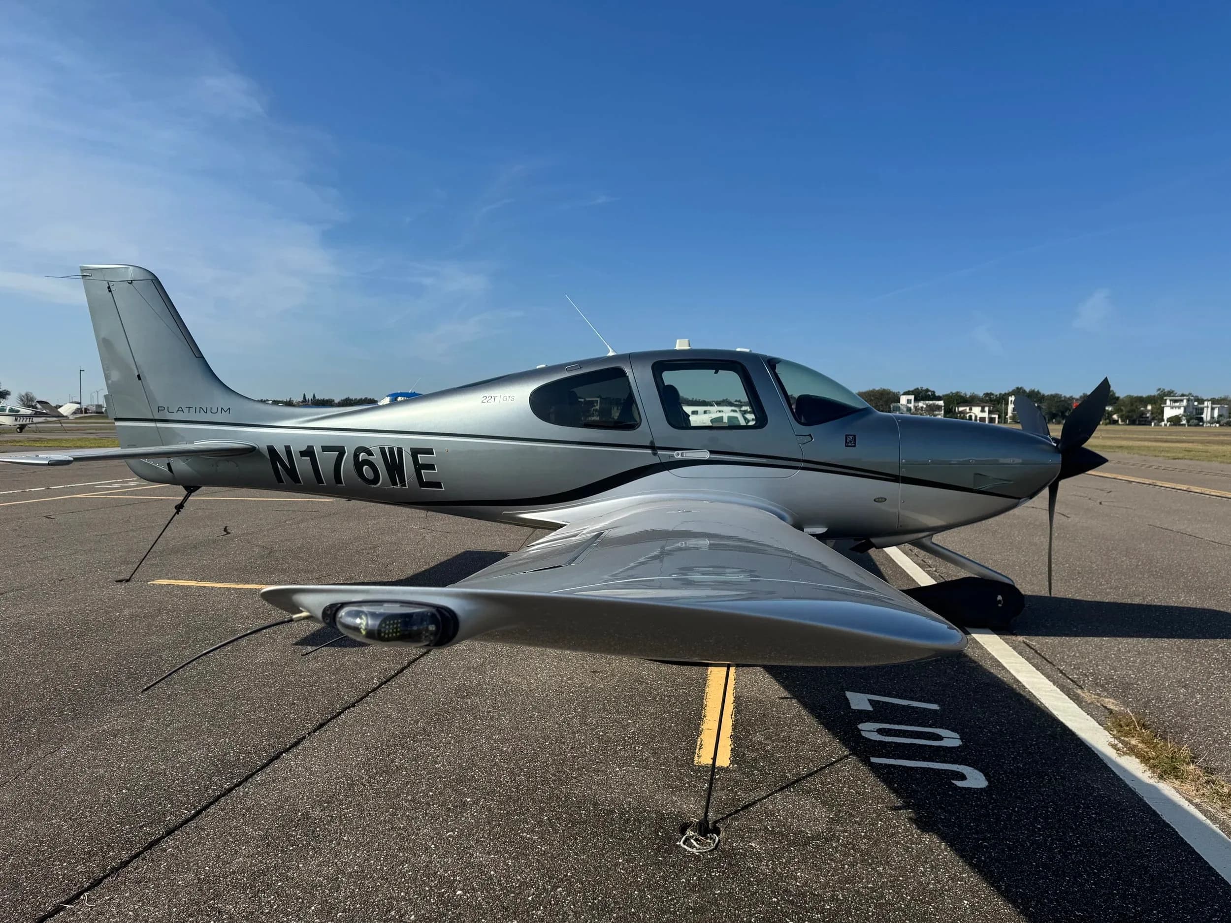 A Cirrus SR22 with a silver paint scheme is parked on the tarmac.