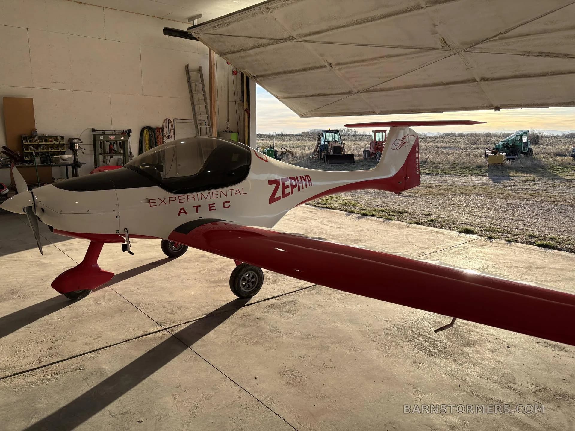 A white and red ATEC Zephyr experimental aircraft is parked inside a hangar, viewed from the front-right side.