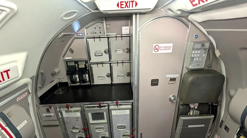 A wider view of an aircraft galley and lavatory door with an overhead exit sign.