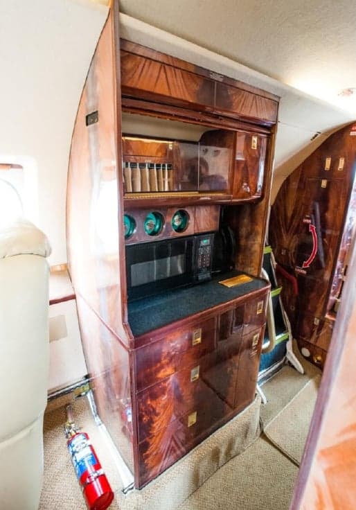 A wooden cabinet with a microwave and storage is visible in the aircraft interior.
