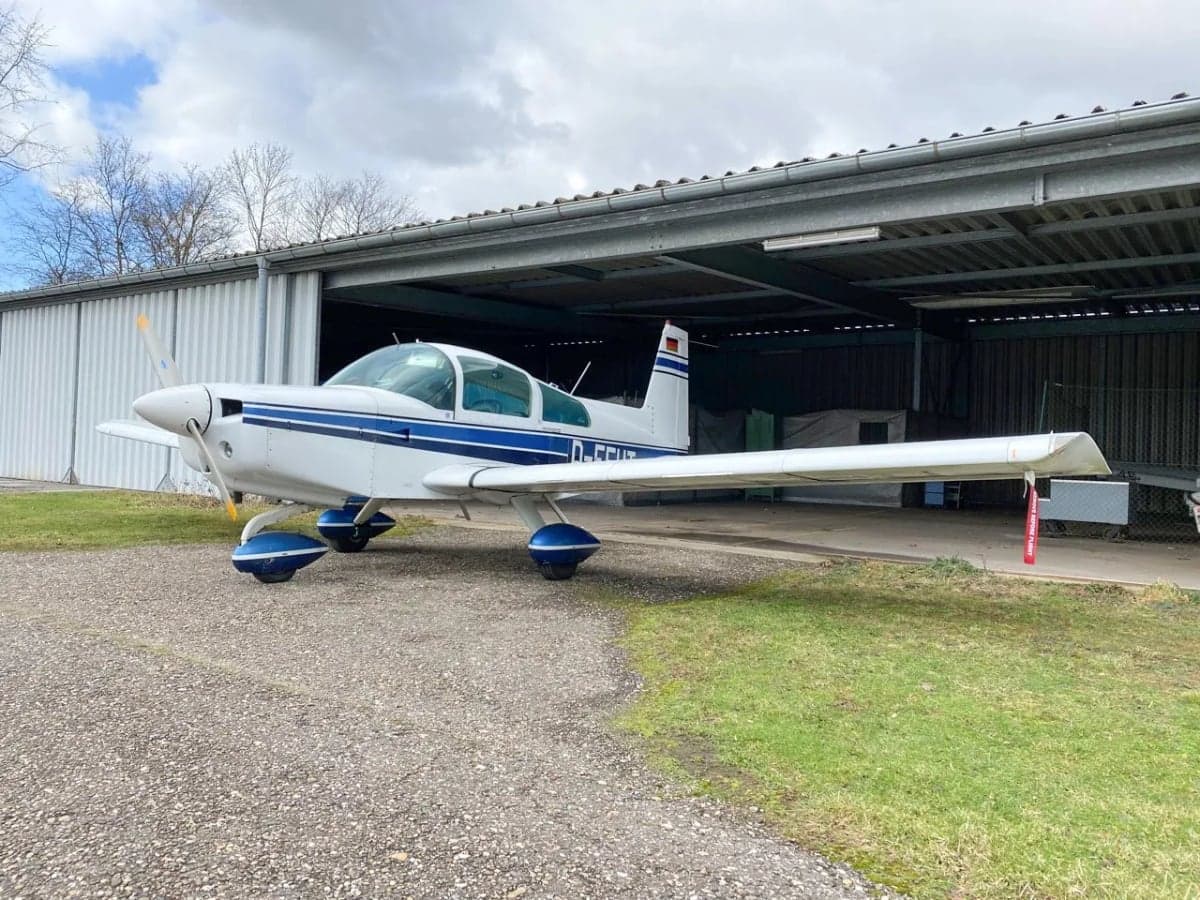 A white and blue aircraft with the registration D-EEHT parked in front of a hangar.