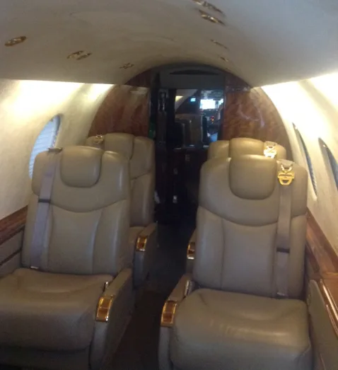 An interior view of an aircraft cabin looking forward, showing beige seats and an aisle.