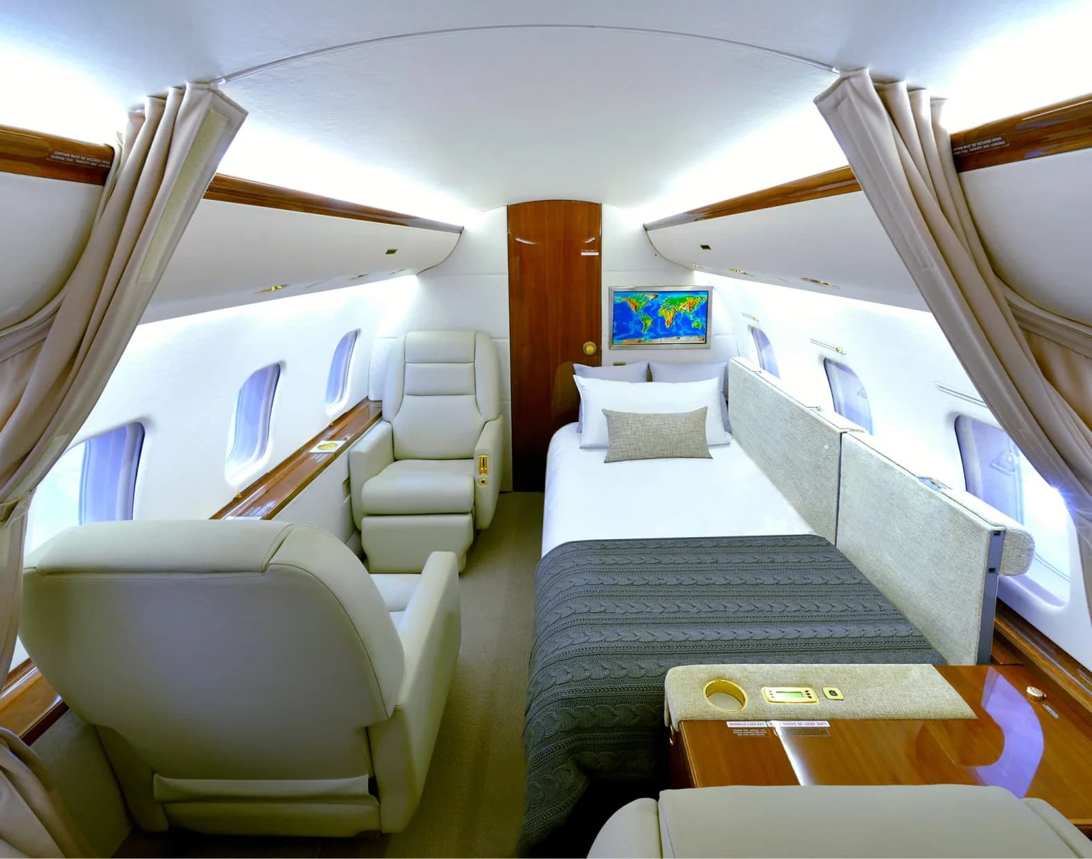 A private jet cabin section featuring a comfortable bed with a grey blanket and an adjacent reclining seat.