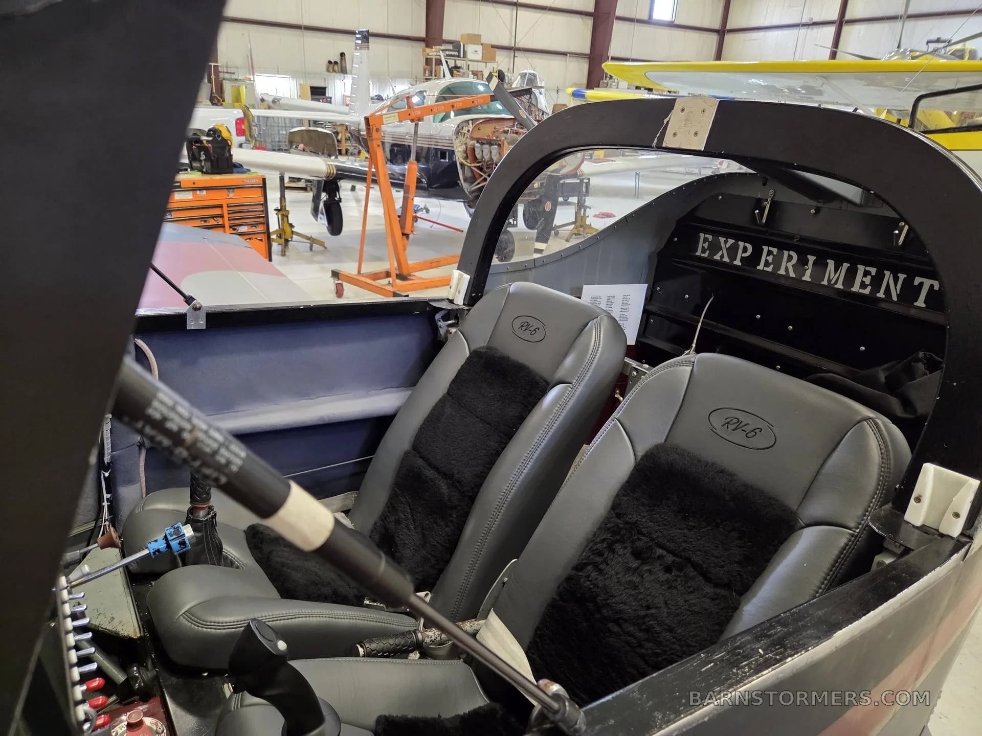The gray leather seats with black fur inserts inside an RV-6 aircraft, with the canopy open in a hangar.