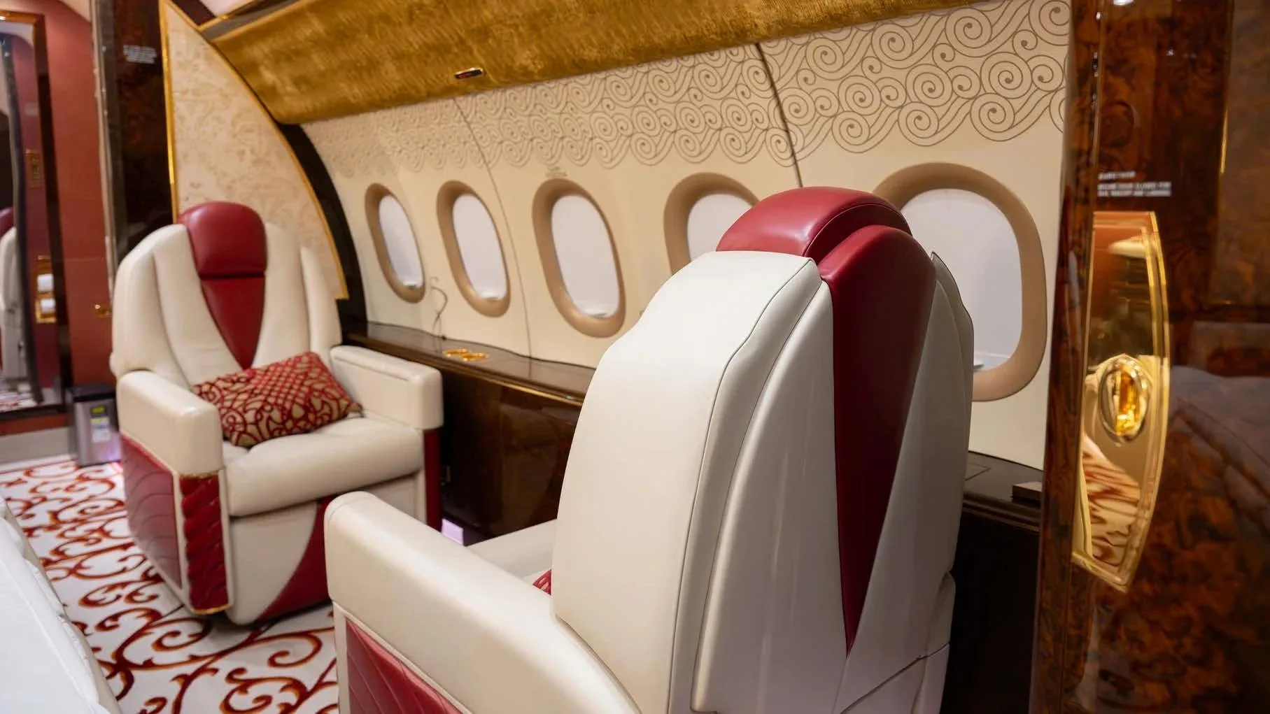 A luxurious aircraft cabin interior with cream and red leather seats and ornate wall patterns.