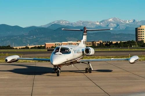 A Learjet 31A with registration N499BS is parked on the tarmac with mountains in the background.