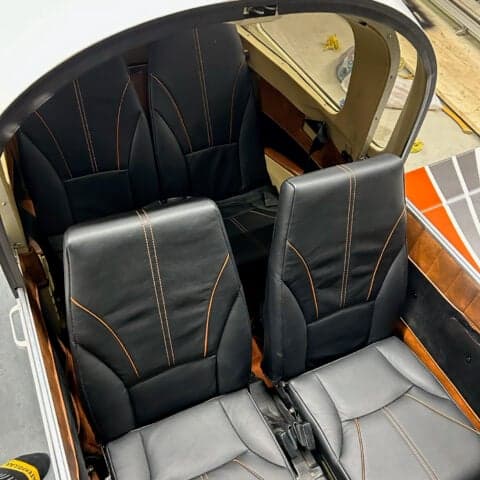 The interior of an aircraft with black leather seats and orange stitching.
