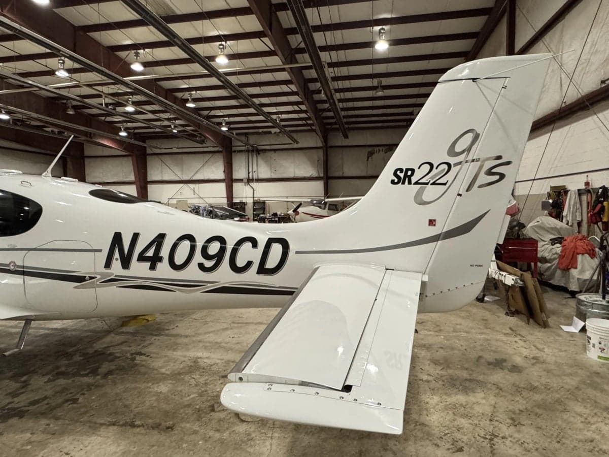 Rear side view of a Cirrus SR22T in a hangar, showing the tail and registration number N409CD.
