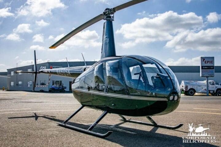 Robinson R44 helicopter on the tarmac with a dark green paint scheme.