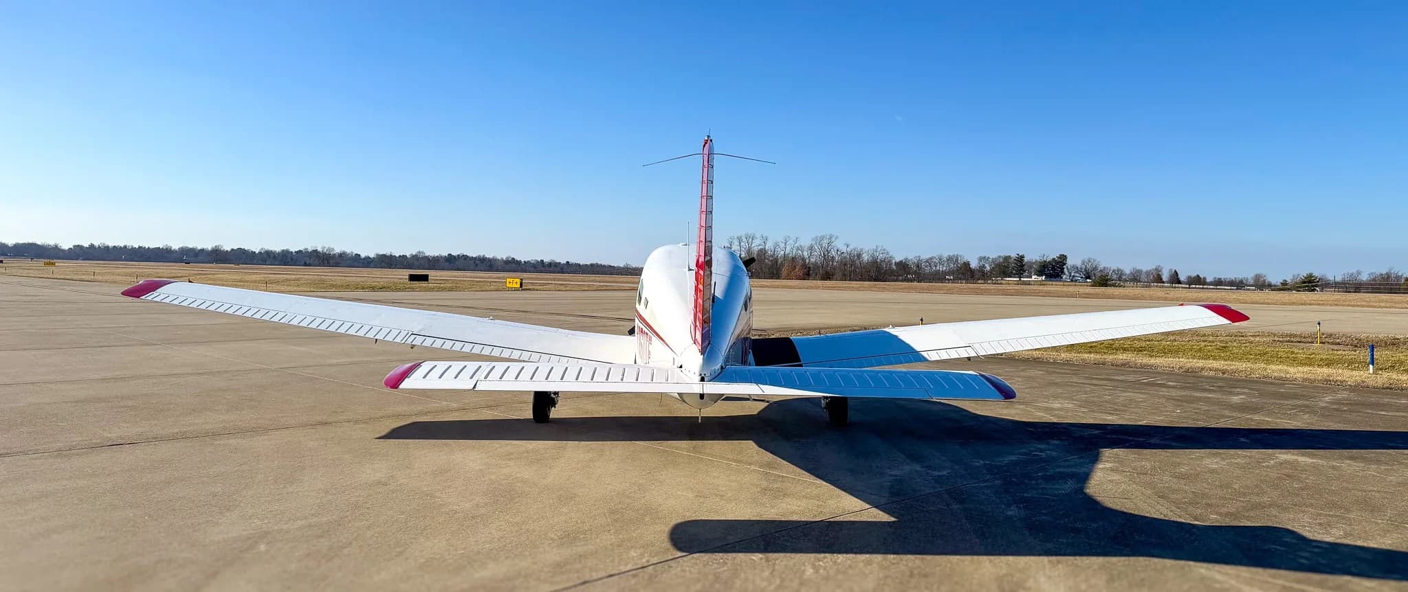 A rear view of a red and white Piper Archer TX aircraft, tail number N161TF, parked on an asphalt tarmac.