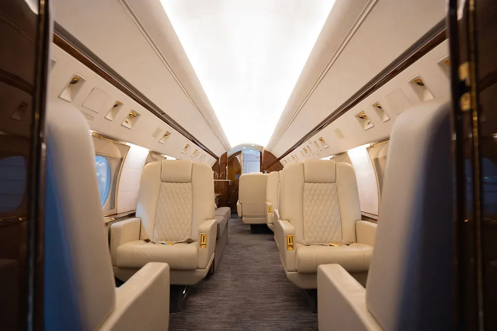 A view down the aisle of a private jet cabin with cream leather seats and overhead lighting.