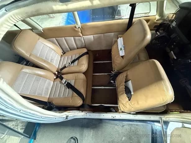 The tan and beige interior cabin of a small aircraft, showing four seats with seatbelts.