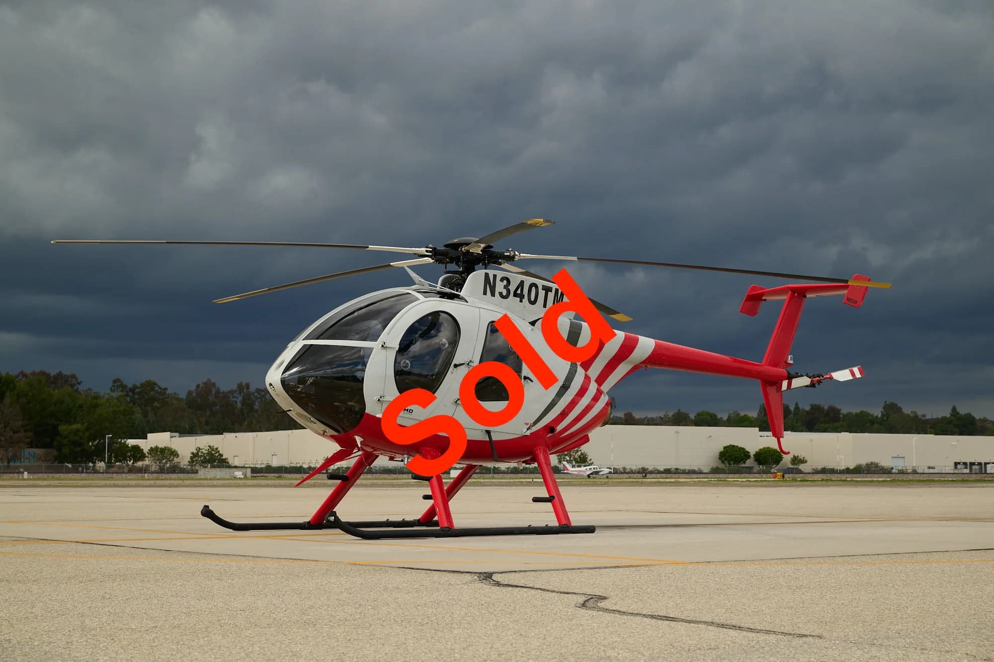 A white and red MD 500 series helicopter with registration N340TM sits on an airfield under a cloudy sky, with 'SOLD' overlaid.