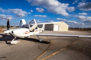 A Cirrus SR22 aircraft with a custom paint scheme is parked on the tarmac with its doors open.