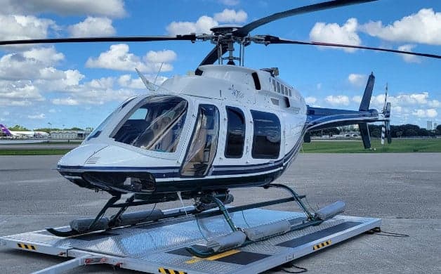A white and blue Bell 407 helicopter on a trailer.