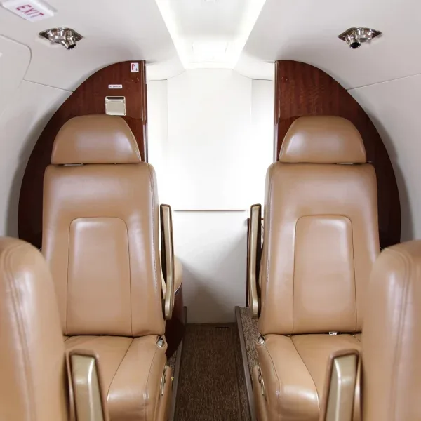 A view of the rear cabin of a private jet with tan leather seats and a light-colored bulkhead.
