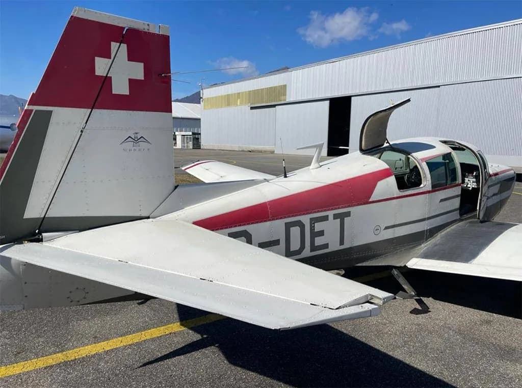 A close-up view of the tail and open doors of the white and red aircraft HB-DET, showing the Swiss flag on the tail.
