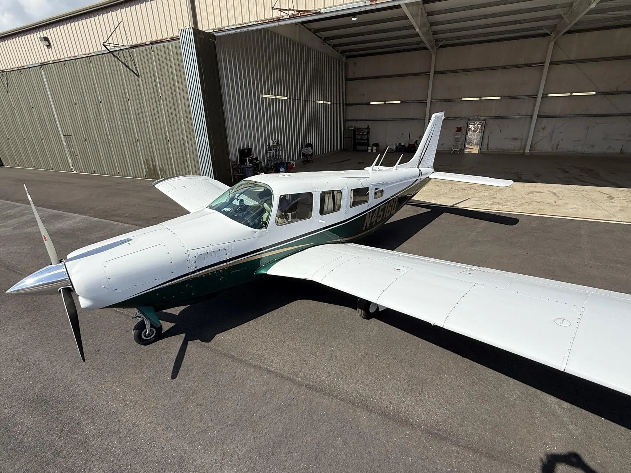 A white and green single-engine propeller aircraft, N4518Q, is parked on an asphalt apron in front of an open hangar.