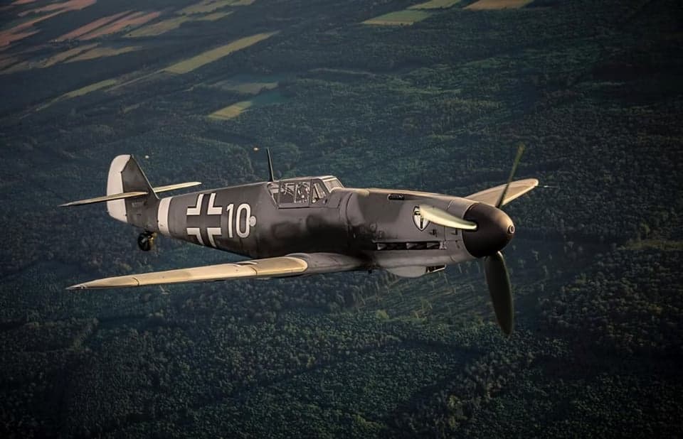 A gray Messerschmitt Bf 109 aircraft in flight at sunset.
