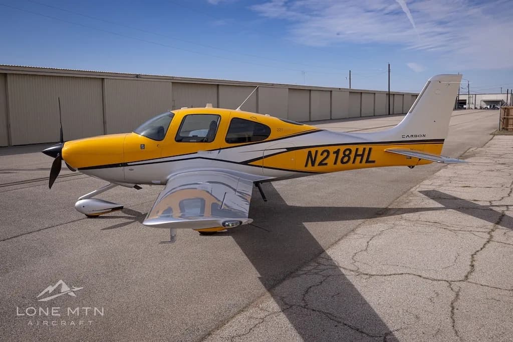 A Cirrus SR22 aircraft with yellow and silver paint scheme parked on an airfield, showing the right side.