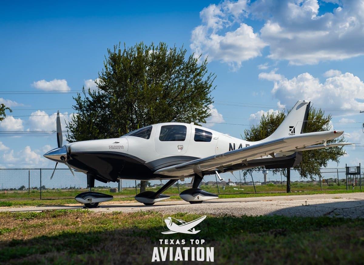 A Cirrus aircraft is parked on the tarmac with a gray and white paint scheme.