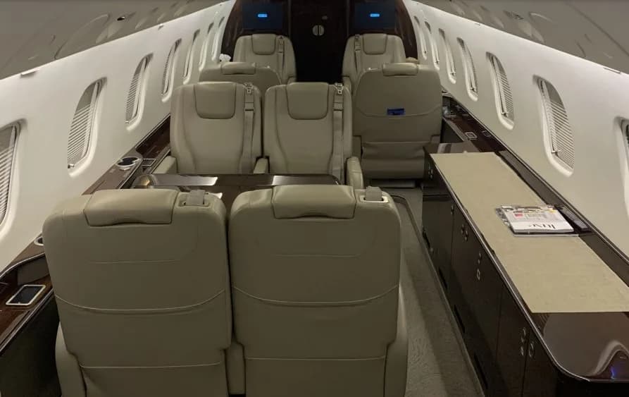 The aircraft cabin interior looking aft, featuring multiple beige leather seats and a long side console.