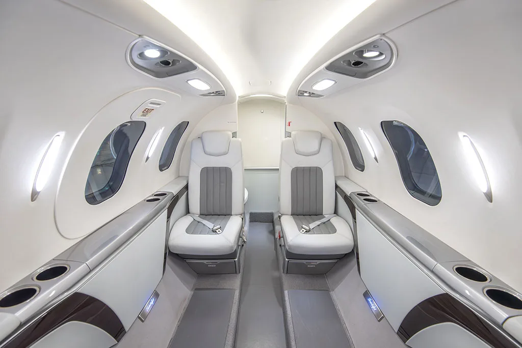 The interior cabin of a HondaJet HA-420, showing two rows of white and grey leather seats facing forward.