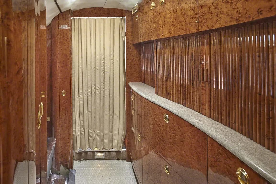 A view of the aircraft's galley or storage area with polished wood cabinetry and a privacy curtain.