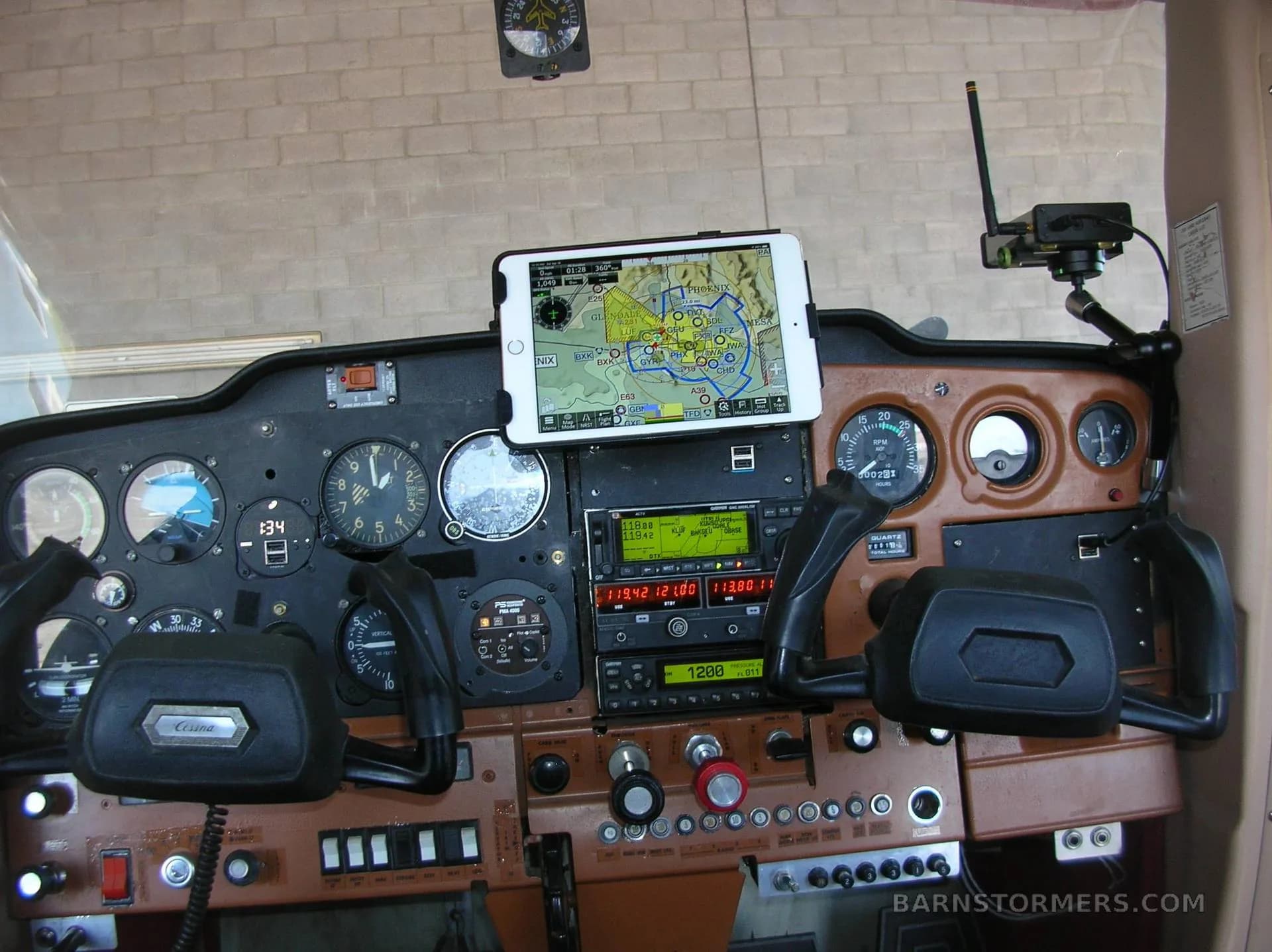 The cockpit of a small aircraft, showing the instrument panel, yokes, avionics, and a tablet displaying a navigation map.