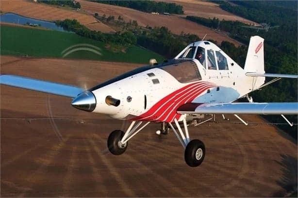 A white and red Thrush 510G crop duster aircraft flying low over agricultural fields.
