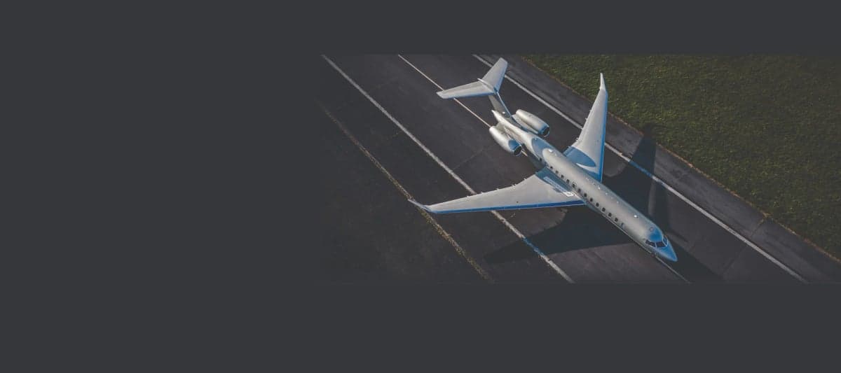 An aerial view of a silver business jet with a blue stripe on a runway, partially obscured by a dark grey overlay.