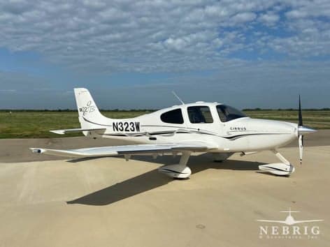 A white Cirrus SR22 aircraft with black accent stripes is parked on a tarmac under a partly cloudy sky.