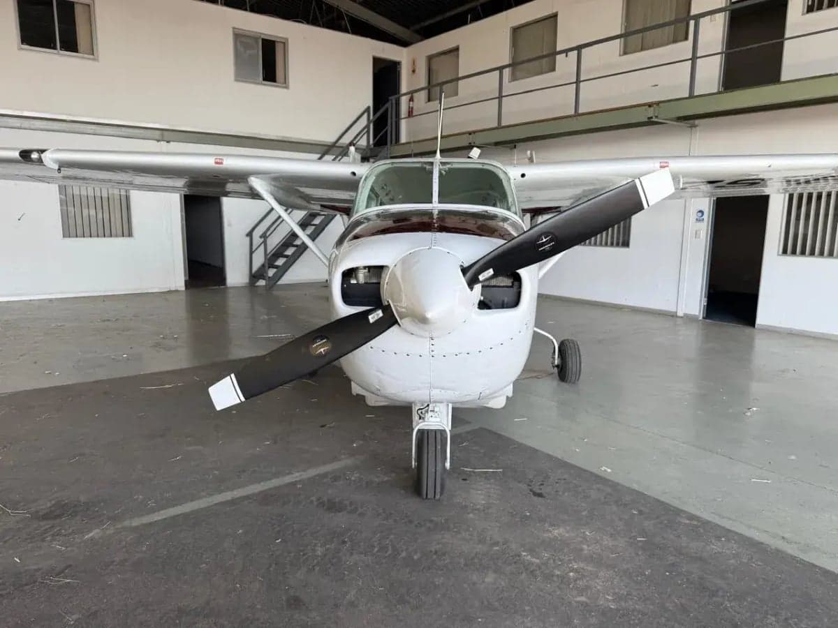 Front view of a white and maroon single-engine propeller aircraft with a three-blade propeller, parked in a hangar.