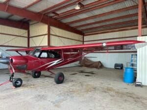 A red Cubcrafters aircraft is parked in a hangar.