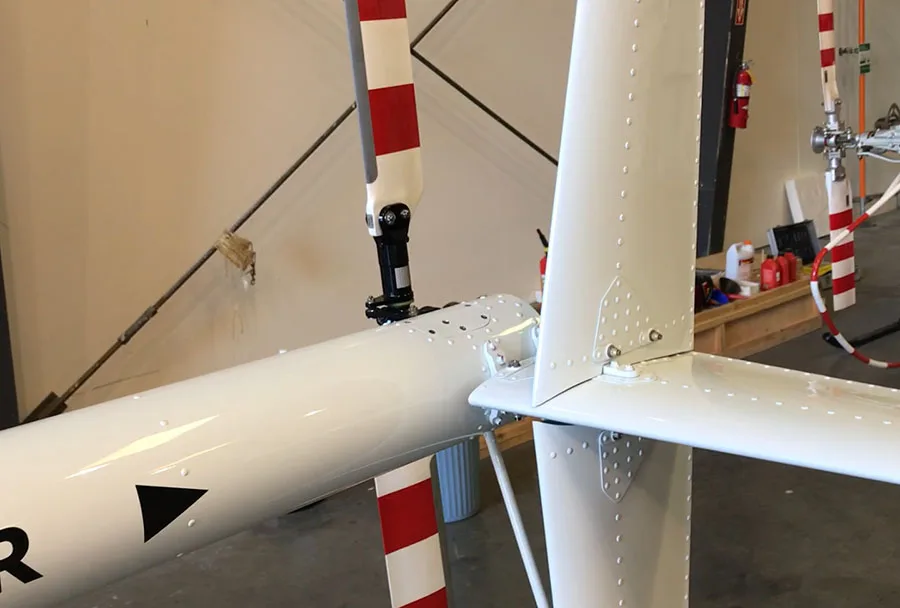 Close-up view of the white tail boom and red-and-white striped tail rotor of a helicopter inside a hangar.