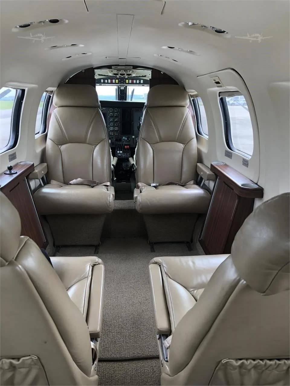 The interior of a private aircraft cabin, featuring four beige leather seats and a view towards the cockpit.