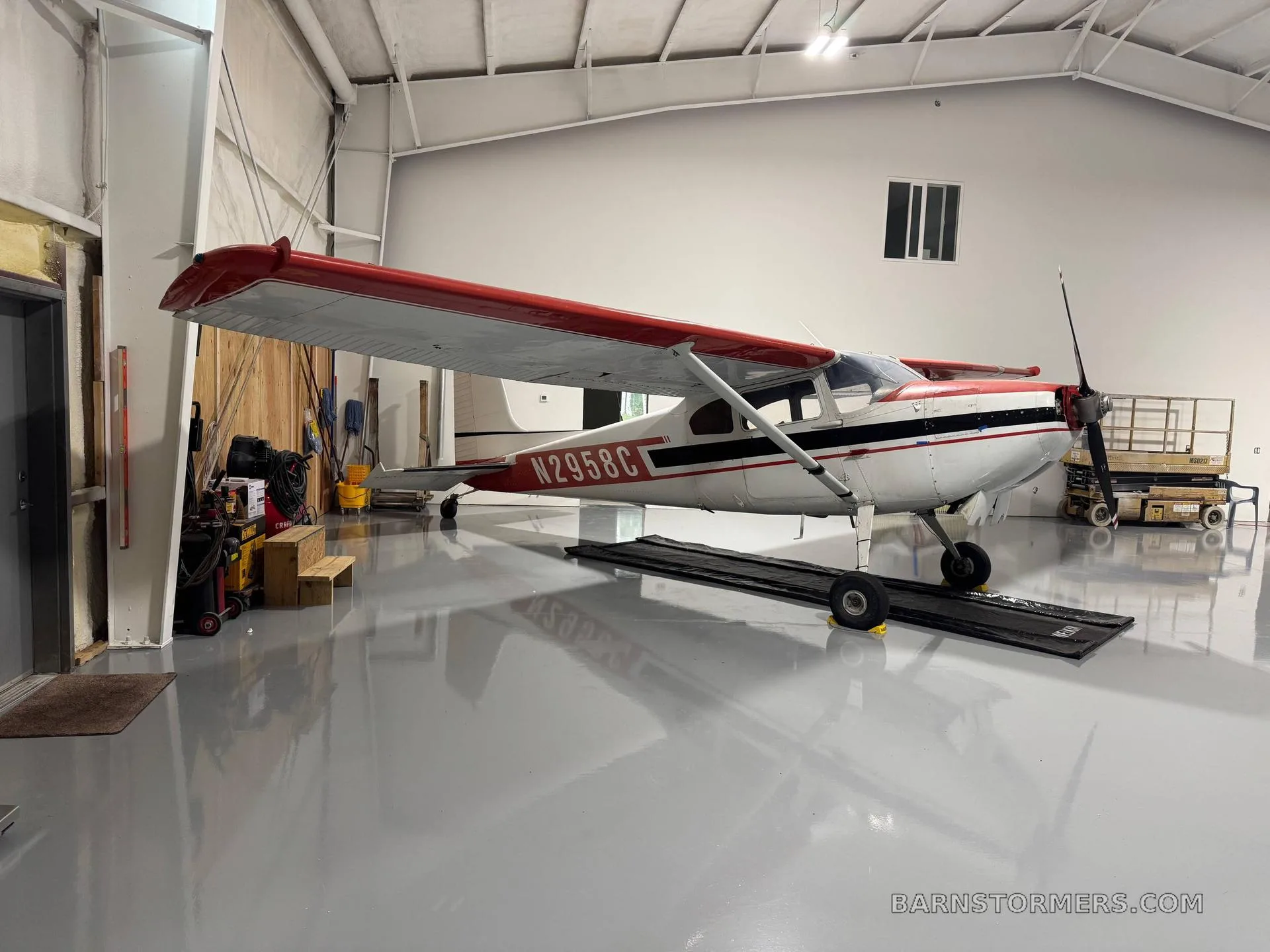 A white and red aircraft (N2958C) with conventional landing gear parked inside a clean, modern hangar.