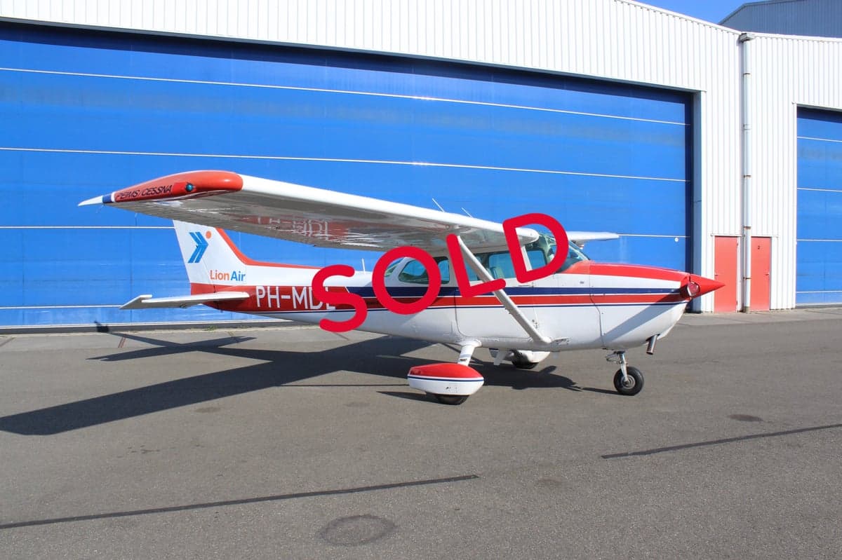 A Cessna 172 aircraft with a red and white paint scheme is parked in front of a blue hangar, with a 'SOLD' overlay.