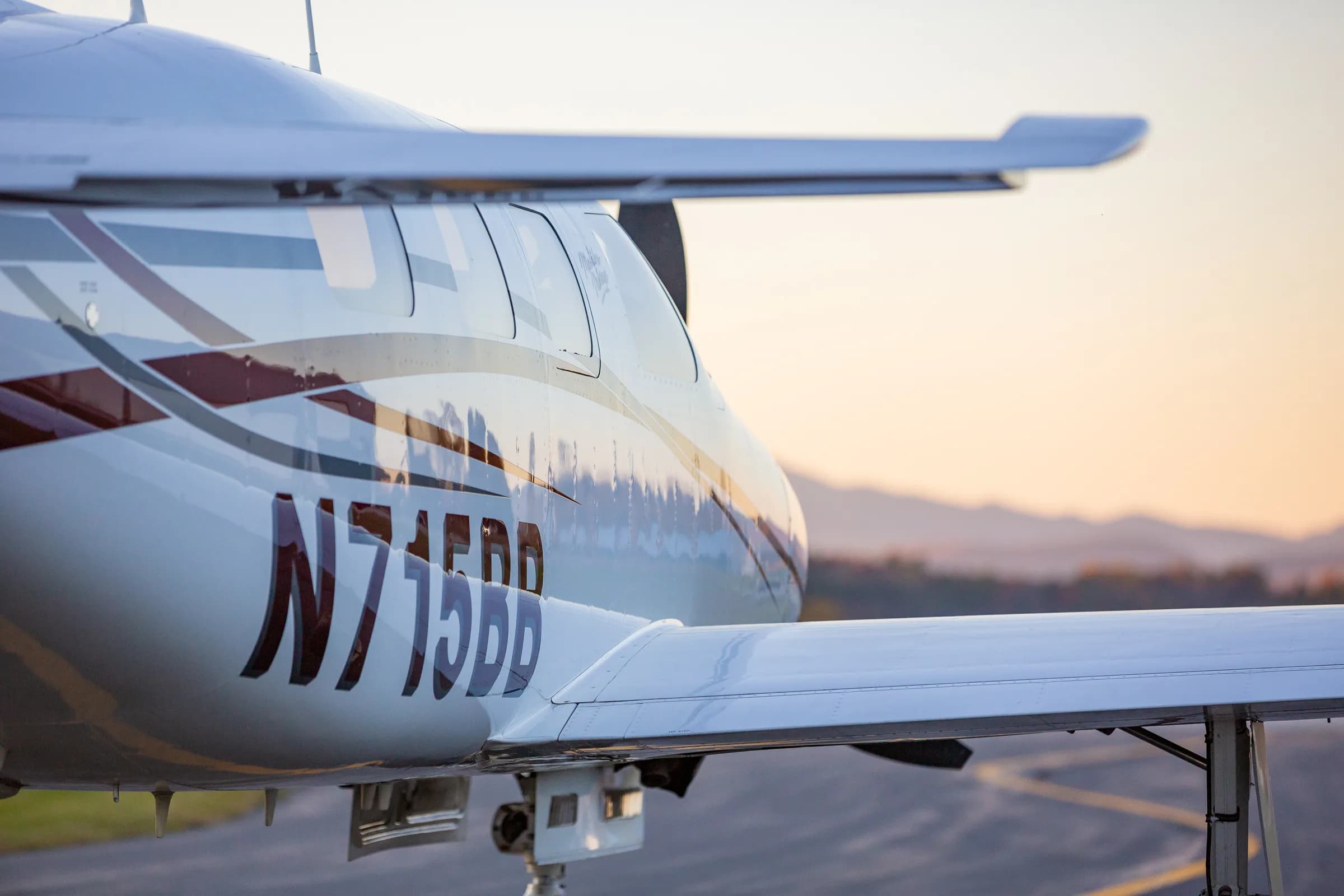 A close-up of the fuselage and wing of Piper Malibu Mirage N715BB with mountains in the background.