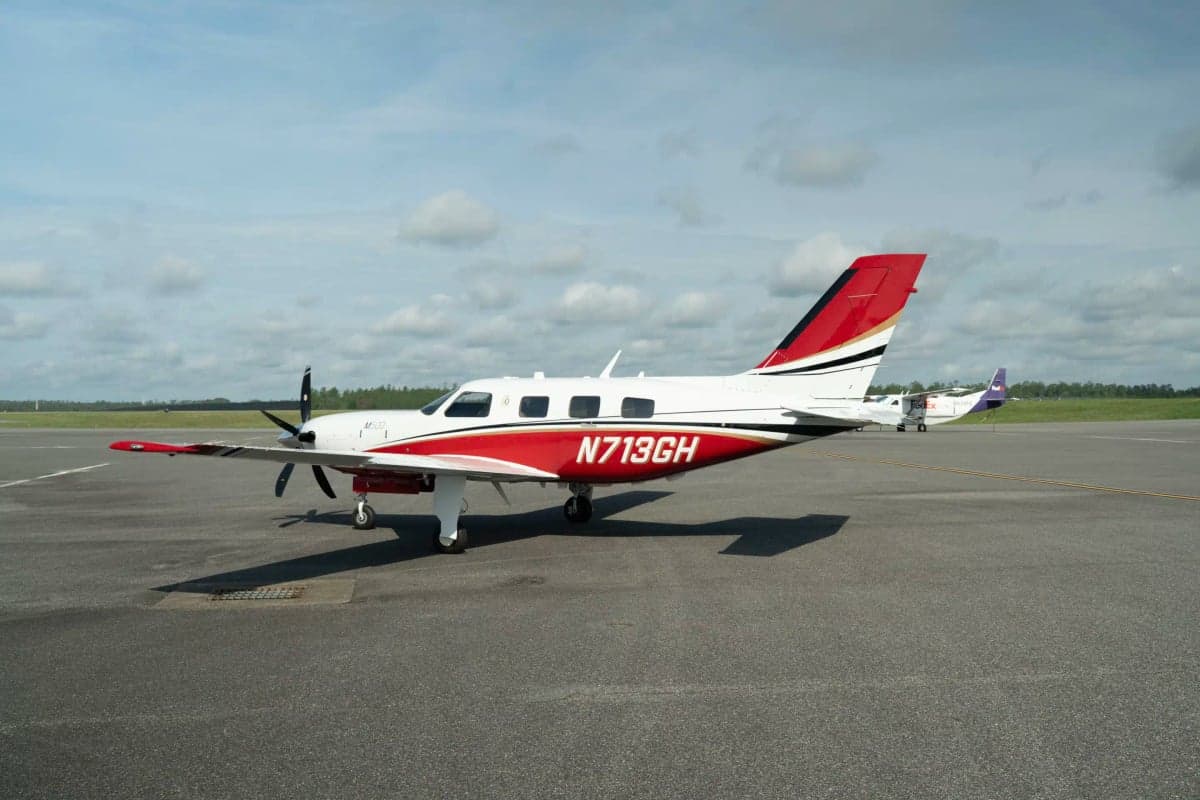 A white and red Piper M500 aircraft with registration N713GH parked on an asphalt tarmac with a FedEx plane in the background.