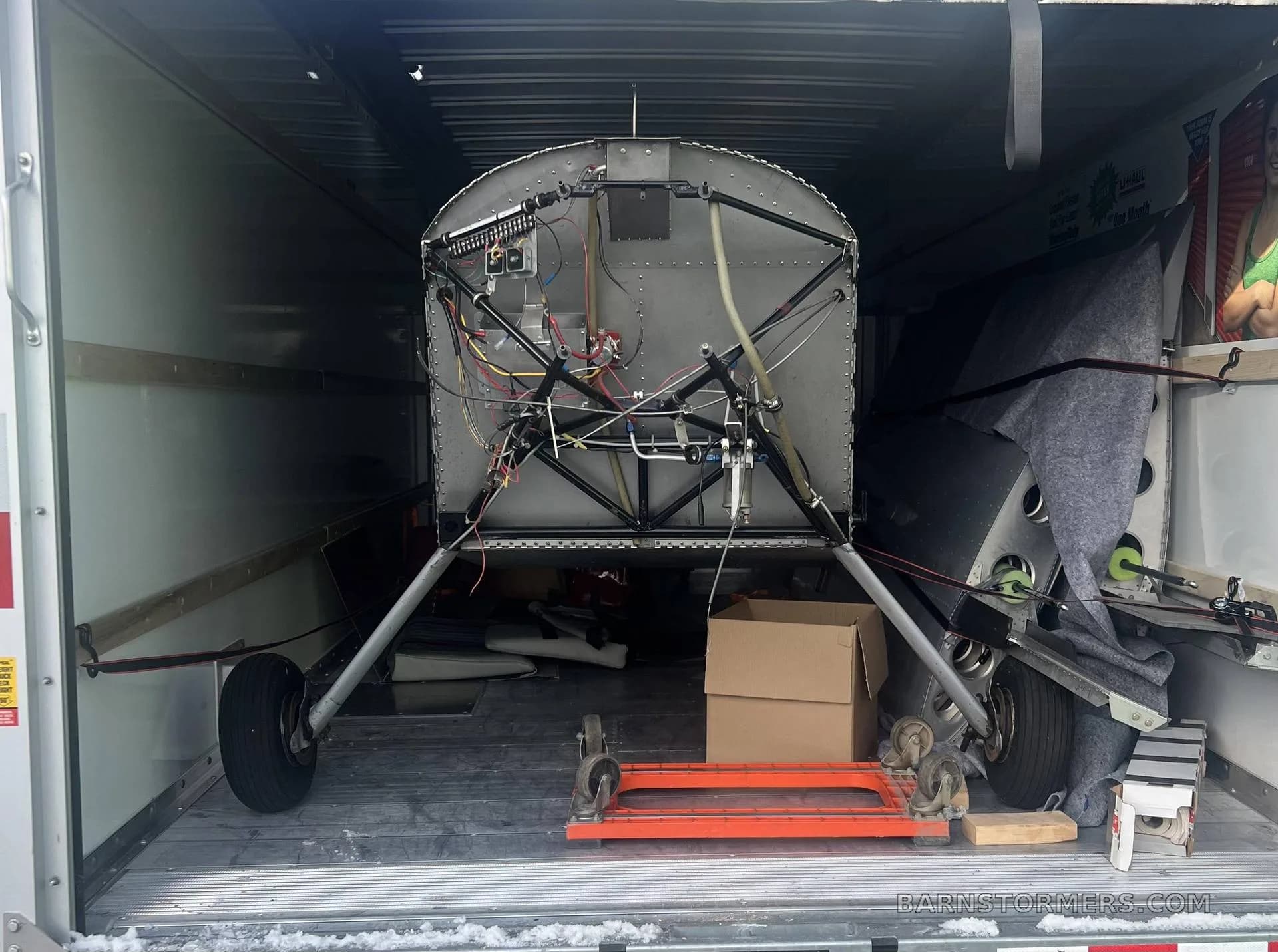 The front fuselage frame of a disassembled aircraft with landing gear, stored inside a trailer.