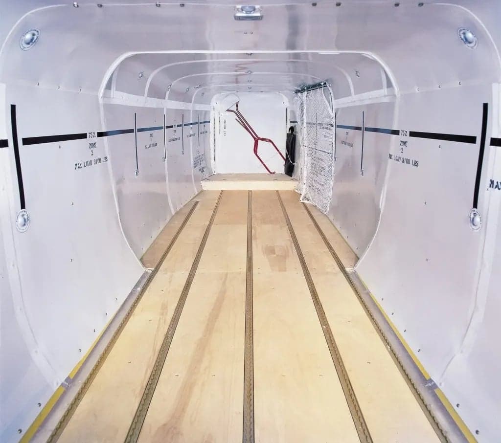 Empty cargo area of an aircraft with wooden floor and metal walls.