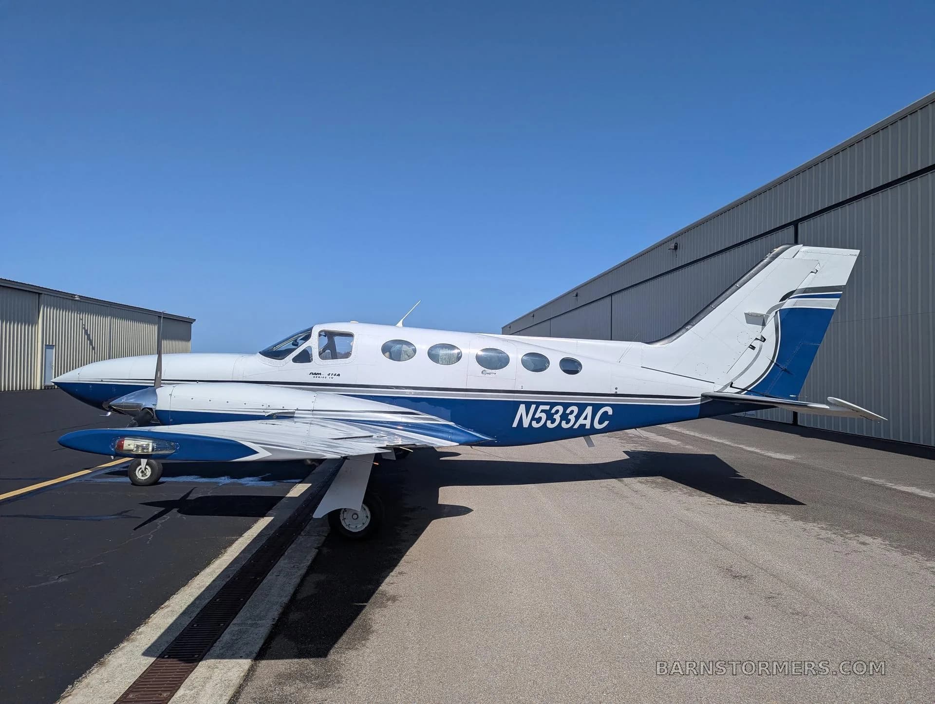 A white and blue twin-engine propeller aircraft (Cessna 414 Chancellor) with tail number N533AC parked on an asphalt ramp, viewed from the front-right side.