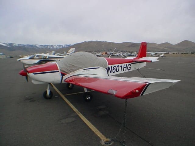A red and white light sport aircraft N601HG, with a cockpit cover, is parked on an airfield.
