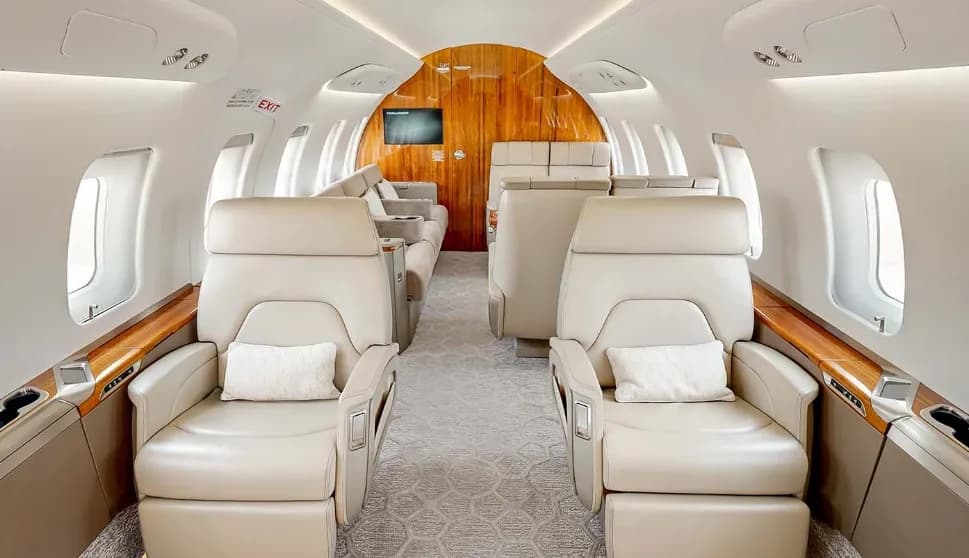 The luxurious main cabin of a private jet featuring beige leather seats and polished wood accents.